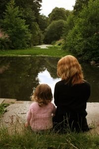 Mother and daughter sitting by a pond